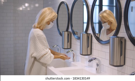 Senior woman in safety mask washing hands with soap in public restroom