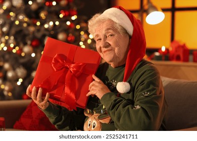 Senior woman in Santa hat with gift at home on Christmas eve - Powered by Shutterstock