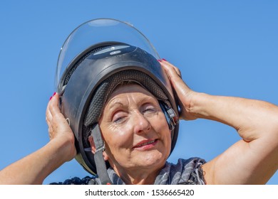 Senior Woman With Scarf On Her Neck Putting On Black Motorcycle Helmet With Blue Sky In Background