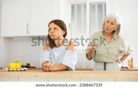 Senior woman scolding her adult daughter cooking breakfast in kitchen