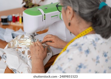 Senior woman sewing patterned fabric on a sewing machine, focusing intently on her task. Concept of sewing craftsmanship - Powered by Shutterstock