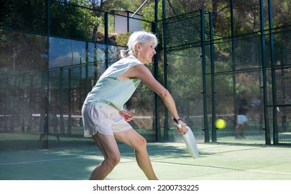 Senior woman in shorts playing padel tennis on court. Racket sport training outdoors. - Powered by Shutterstock