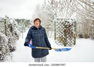 Senior Woman Shoveling Snow Off A Walkway After Massive Snowfall. Winter Chores.