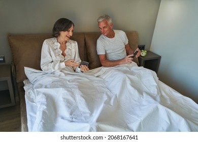 Senior Woman Showing Her Phone Screen To Man In Bed