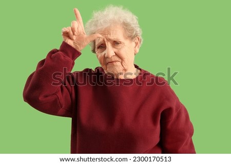 Senior woman showing loser gesture on green background