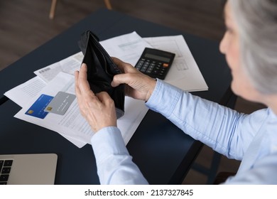 Senior woman sit at desk opening empty purse, no banknotes, without coins inside after pay bills and taxes, above top view. Financial crisis, bankruptcy, low pension of older citizen, poverty concept