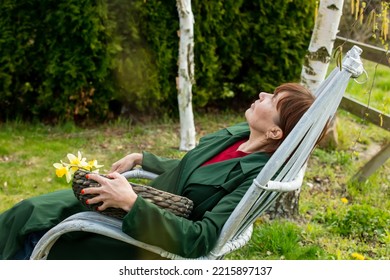 Senior Woman Sits In Armchair In Spring Time Garden