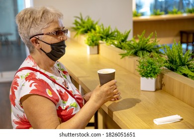 Senior woman sitting in the airport waiting area wearing handmade face mask trying to drink coffee to go. Travel restrictions due to coronavirus outbreak concept - Powered by Shutterstock