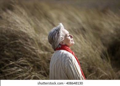 A senior woman sitting amongst the sand dunes, enjoying the sun