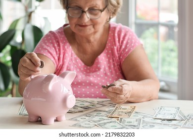 Senior Woman Sitting At Desk Putting Money Coins Inside Piggy Ba