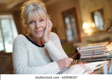 Senior woman sitting at desk and writing on book