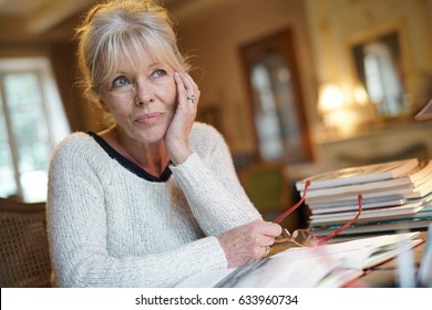 Senior Woman Sitting At Desk And Writing On Book