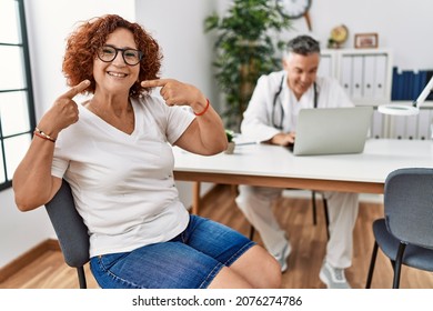 Senior Woman Sitting At Doctor Appointment Smiling Cheerful Showing And Pointing With Fingers Teeth And Mouth. Dental Health Concept. 