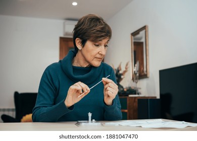 Senior woman sitting at home, studying the instructions for a self test for COVID-19 with Antigen kit on hand. Holds a nasal swab for possible infection of Coronavirus. Health services online.