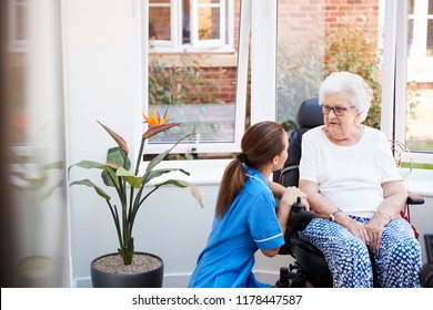 Senior Woman Sitting In Motorized Wheelchair Talking With Nurse In Retirement Home