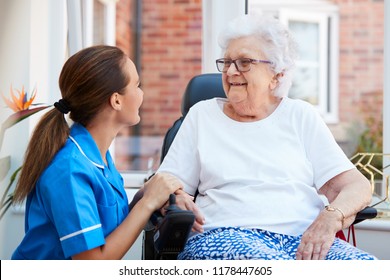 Senior Woman Sitting In Motorized Wheelchair Talking With Nurse In Retirement Home