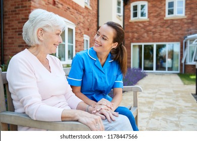 Senior Woman Sitting On Bench And Talking With Nurse In Retirement Home