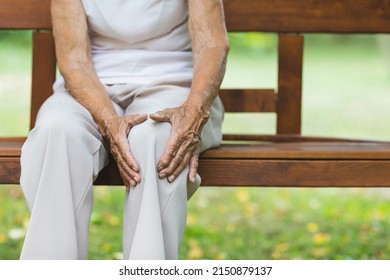 Senior Woman Sitting On Bench, Holding Her Painful Knee