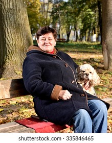 Senior Woman Sitting On A Bench With A Dog In Autumn Park