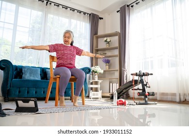 Senior woman sitting on chair and spread both arms and jog in the side to stretch the arm muscles, for good healthy with training exercise online on tablet, workout online from home concept