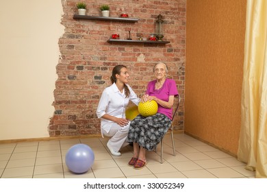 Senior Woman Sitting On A Chair And Holding Spiky Ball During Physiotherapy, Looking At Camera