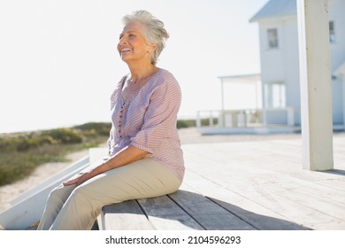 Senior Woman Sitting On Deck Outside Beach House