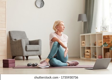 Senior Woman Sitting On The Floor On Exercise Mat In Front Of Laptop And Training At Home