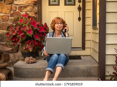 Senior Woman Sitting On Front Porch Of Her House With A Laptop Computer And Smiling Animatedly On Summer Evening In Midwest