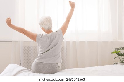 Senior woman sitting on her bed in morning, stretching with arms raised, back view, free space - Powered by Shutterstock