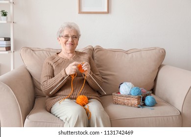 Senior woman sitting on sofa while knitting sweater at home - Powered by Shutterstock