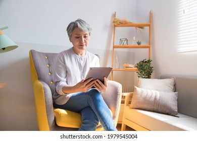 Senior Woman Sitting On A Sofa And Using Tablet At Home.