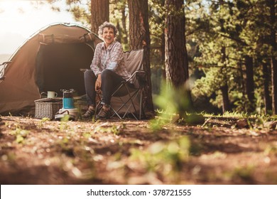 Senior Woman Sitting Relaxed Outside A Tent. Smiling Mature Woman Camping In Forest.