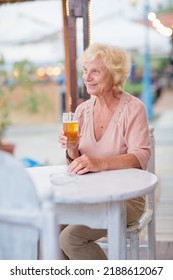 Senior woman sitting at a table in a summer cafe and drinking beer from a tall glass