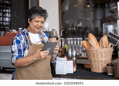 senior woman small business owner Checking the store's sales with a tablet, sipping coffee, having a smiling face, happy because the profit exceeds expectations.expand more branches open online market - Powered by Shutterstock