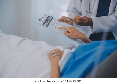 The senior woman specialist doctor with stethoscope checking up happy young Asian female patient lying in bed with receiving an intravenous saline drip in recovery room. Healthcare, medical insurance. - Powered by Shutterstock