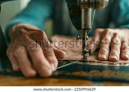 Senior woman in spectacles use sewing machine. wrinkled hands of the old seamstress.elderly woman . Old sewing machine Classic retro style manual sewing machine ready for sewing work. 