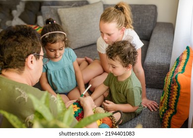 Senior Woman Spending Day With Her Grandchildren, Knitting Granny Square At Home. Two Girls, Grandmother And A Funny Curly Boy Knits Crochet, It's An Old Fashioned Hobby That They Love To Do.