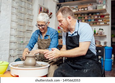 Senior woman spinning clay on a wheel with a help of a teacher at pottery class - Powered by Shutterstock