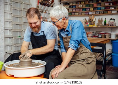 Senior woman spinning clay on a wheel with a help of a teacher at pottery class - Powered by Shutterstock