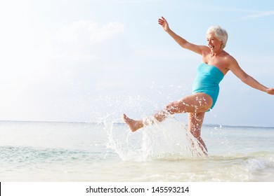 Senior Woman Splashing In Sea On Beach Holiday - Powered by Shutterstock