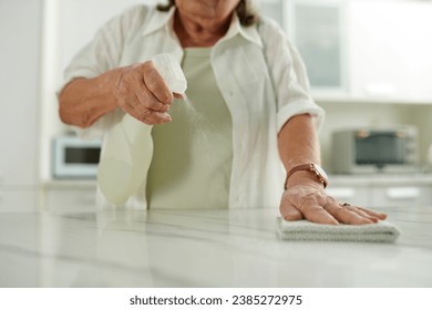 Senior woman spraying detergent on kitchen counter when cleaning house - Powered by Shutterstock