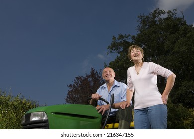 Senior Woman Standing Next To Man On Riding Lawn Mower