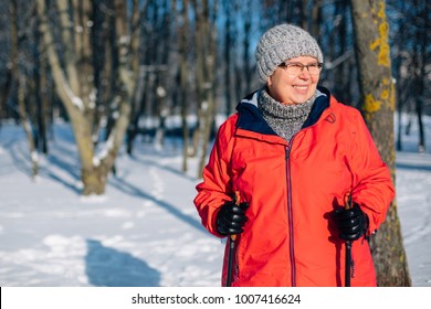 Senior Woman Standing With Nordic Walking Poles In Winter  Park. Healthy Lifestyle Concept. Mature Woman Resting After Exercise Outdoors.