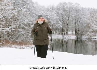 Senior Woman Standing With Nordic Walking Poles In Winter  Park. Healthy Lifestyle Concept. Mature Woman Resting After Exercise Outdoors.