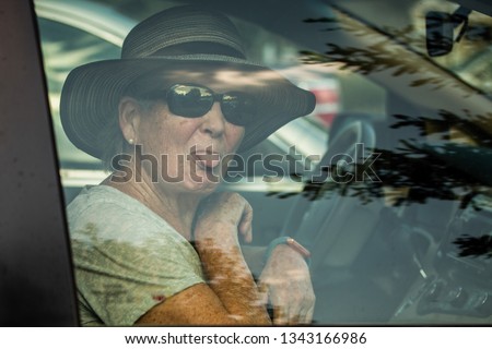 Senior Woman Sticks Out Her Tongue While Looking Through a Car Window