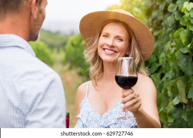 Senior woman with straw hat holding wine glass and looking at camera. Winegrowers at wineyard tasting red wine. Close up face of smiling mature woman raising a glass of red wine. - Powered by Shutterstock