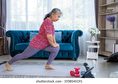 Senior Woman Stretch  Back And Leg Muscles. Reduce Knee Pain, Training Exercise Online With Tablet In Living Room During Quarantine