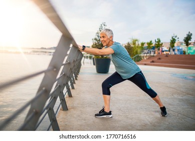 A Senior Woman Stretches During Her Workout. Mature Woman Exercising. Portrait Of Fit Elderly Woman Doing Stretching Exercise In Park. Senior Sportswoman Making Stretch Exercises