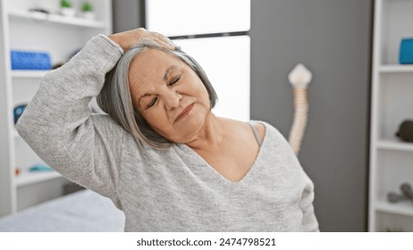 A senior woman stretching her neck indoors at a clinic, showcasing therapy and wellness. - Powered by Shutterstock