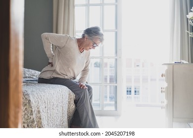 Senior woman suffering from backache after sleep, rubbing stiff muscles, Old female sitting on bed touching lower back feeling discomfort because of uncomfortable bed at home
